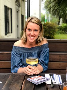 a woman sitting at a table with a glass of wine in front of her smiling