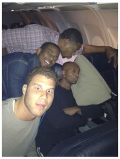 four men sitting on an airplane looking at the camera