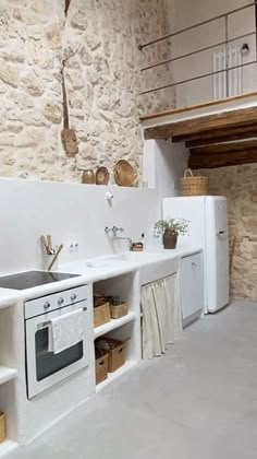 a kitchen with an oven, sink and refrigerator in the corner next to stone walls