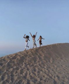 three women jumping in the air on top of a sand dune with their arms up