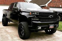 a black chevrolet truck parked in front of a brick house with two cars behind it