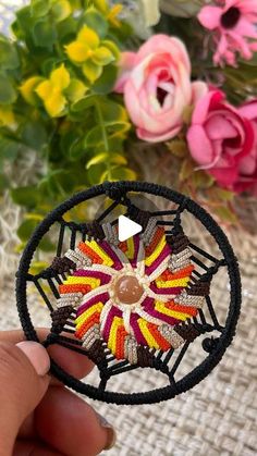 a hand holding a small piece of string art with flowers in the back ground behind it