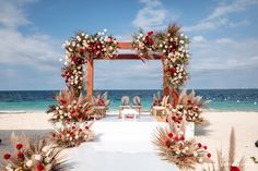 an outdoor ceremony set up on the beach with flowers and greenery in front of it