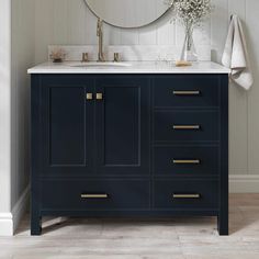 a white sink sitting under a mirror next to a blue cabinet with gold handles and drawers