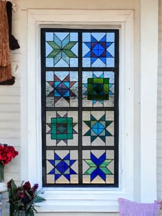 a stained glass window sitting on the side of a white building with flowers in front of it