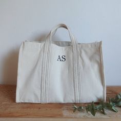 a white canvas bag sitting on top of a wooden table next to an eucalyptus plant