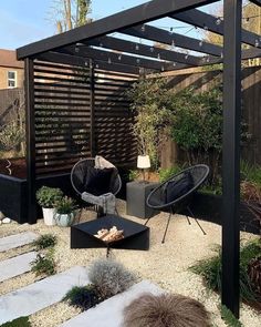 an outdoor patio with chairs, table and fire pit surrounded by plants in the back yard