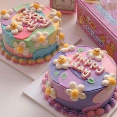 two decorated cakes sitting next to each other on top of a white table with pink boxes