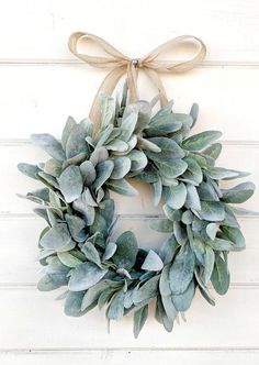 a wreath hanging on the side of a white wall with a brown ribbon around it