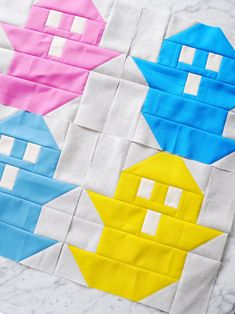 four different colored blocks are arranged on a white table top, with one block in the shape of a house