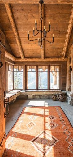 the sun shines through the windows in this rustic living room with wood paneling and chandelier