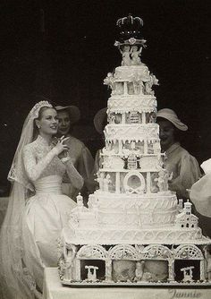 two people standing next to a large white wedding cake