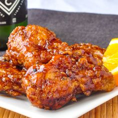 two pieces of chicken sitting on top of a white plate next to an orange slice