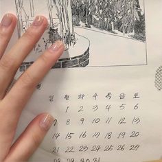 a person's hand on top of a calendar with trees and bushes in the background