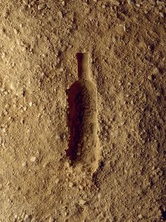 a bottle that is sitting in the sand on the ground with dirt all over it