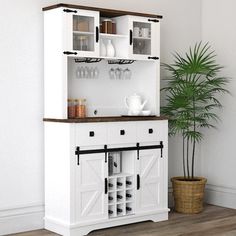 a white hutch with wine glasses on it and a potted plant in the corner