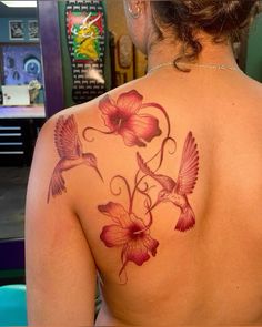 the back of a woman's shoulder with hummingbirds and flowers tattoo on it