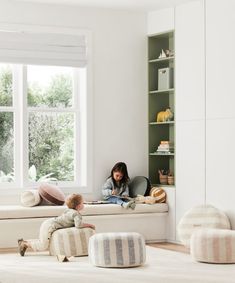 a woman sitting on top of a white couch next to a child in front of a window