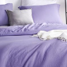 a bed covered in purple sheets and pillows