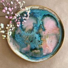 a plate with blue and pink paint on it next to some small white flower stems