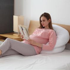 a pregnant woman sitting on a bed reading a book