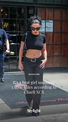 a woman in black pants and crop top walking down the street