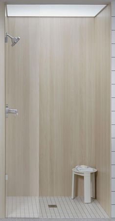 a bathroom with a walk in shower next to a white table and stool on the floor