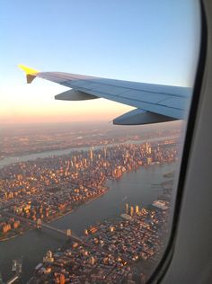 the wing of an airplane flying over a large city and river with lots of tall buildings