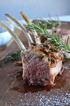 a piece of meat on a wooden cutting board with rosemary sprigs and seasoning