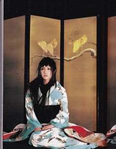 a woman sitting on the ground in front of two birds hanging from a tree branch