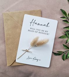 a card that says hannah will you be my maid of honour? with a feather on it