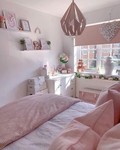 a bed room with a neatly made bed next to a window and a lamp hanging from the ceiling