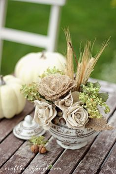 an arrangement of flowers in a bowl on a table with pumpkins and other decorations