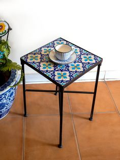 a blue and white table sitting on top of a tiled floor next to a potted plant