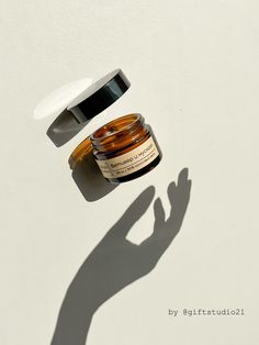 the shadow of a person's hand next to a jar of skin care product