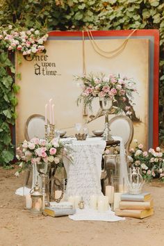 a table set up with flowers and candles for a wedding reception in front of a sign