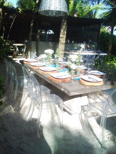 an outdoor dining table set for six with clear chairs and plates on it, surrounded by palm trees