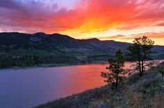 the sun is setting over a lake with mountains in the background and grass on the bank