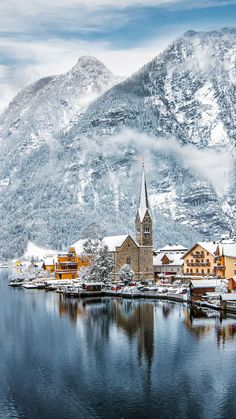 a small town on the shore of a lake with snow covered mountains in the background