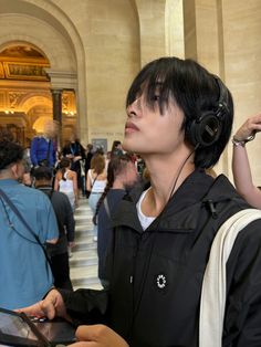 a woman with headphones on looking at something in her hand while holding a tablet