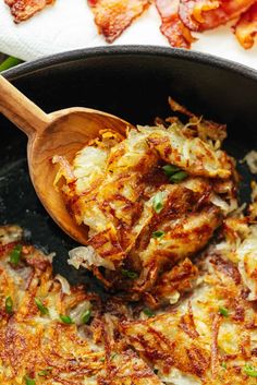 a wooden spoon is scooping food out of a skillet with bacon on the side