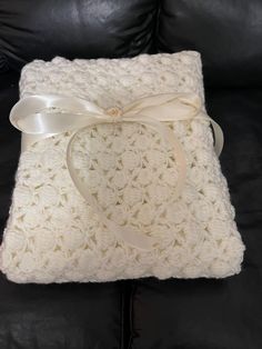 a white crocheted blanket with a bow on it sitting on a black couch