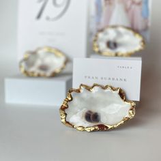 two small white and gold dishes sitting on top of a table next to a card