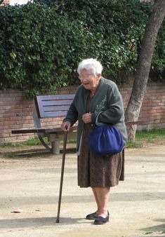 an old woman holding a cane in front of a bench