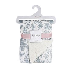 a white and blue floral print blanket with pink ribbon on the bottom, hanging from a hanger