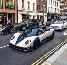 a white and blue sports car driving down a street next to tall buildings with cars parked on both sides