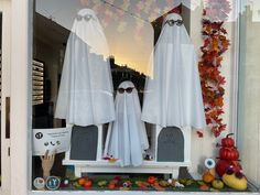 two fake ghost heads are in the window of a halloween store with pumpkins and other decorations