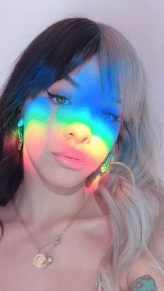 a woman with rainbow makeup and piercings posing for a photo in front of a white wall