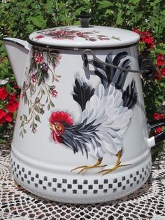 a white and black rooster tea pot sitting on top of a table next to red flowers