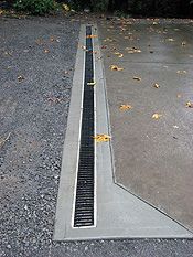 an empty parking lot with a grate on the ground and trees in the background